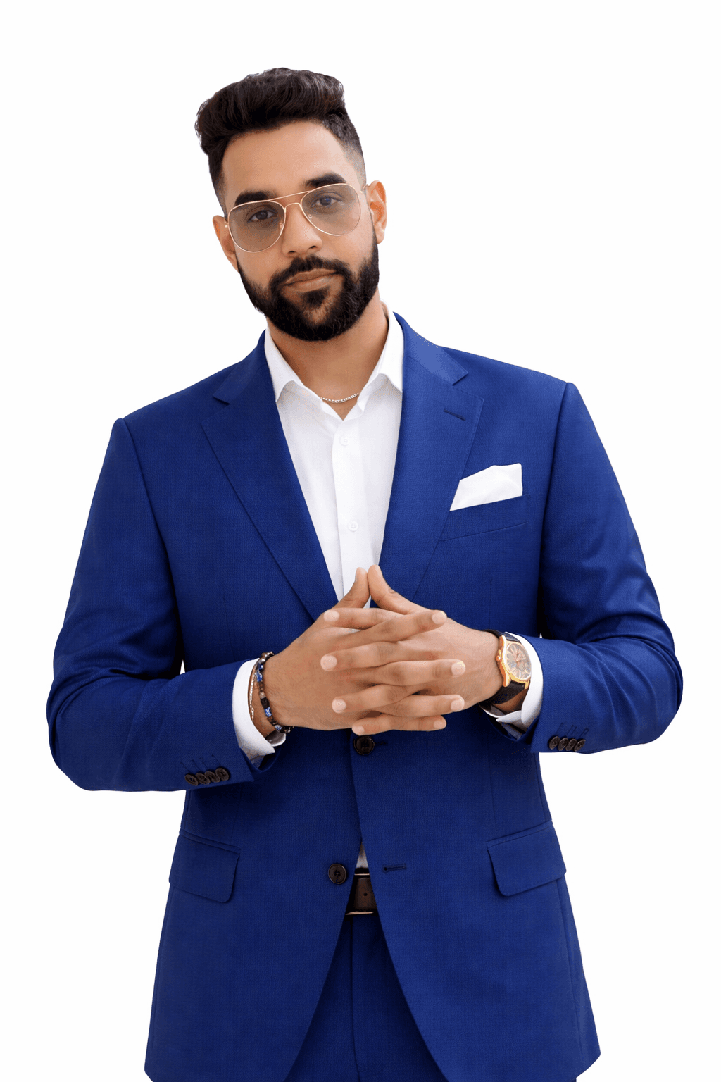 Bearded man in a blue suit and glasses posing with hands clasped against white background.